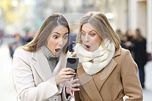 Surprised women reading phone content in winter in the street