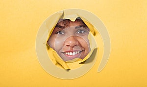Surprised young African American woman looking playfully in torn paper hole, has excited cheerful expression, looks through