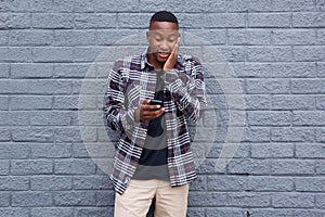 Surprised young african guy looking at cell phone