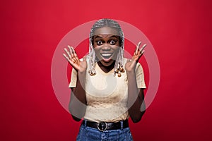 Surprised young african woman covering her mouth isolated on red background