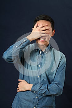 Surprised young Asian man covering his face by palm