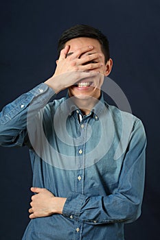 Surprised young Asian man covering his face by palm