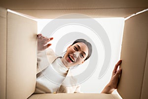 Surprised young asian woman unpacking. Opening carton box and looking inside