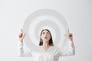 Surprised young beautiful brunette businesswoman smiling looking pointing fingers up over white background.