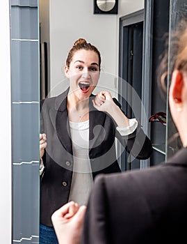 Surprised young beautiful business woman laughing in front of mirror