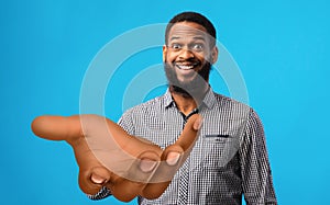 Surprised young black man standing with big outstretched hand on blue studio background, mockup for your product