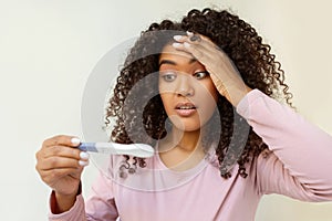 Surprised young black woman holding pregnancy test and looking with disbelief