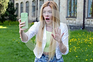 Surprised young blonde woman looks into her smartphone