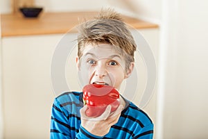 Surprised young boy biting into a red bell pepper