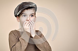 Surprised young boy with cap covering his mouth with hands