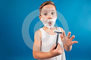 Surprised young boy in shaving foam like man holding razor