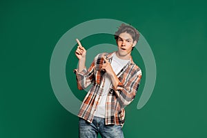 Surprised young boy, teen in casual style clothes posing isolated over green studio background. Back to school, emotions