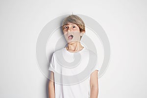 Surprised young boy in white T-shirt posing in front of white empty wall. Portrait of fashionable male child. Smiling