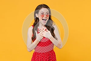 Surprised young brunette woman girl in red summer dress, eyeglasses posing isolated on yellow wall background studio