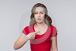 Surprised young brunette woman points to herself index finger, wonders why she was accused of what she did not do