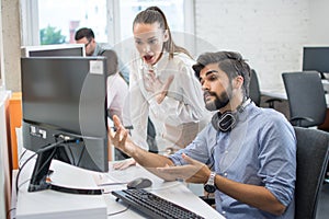 Surprised young business woman and handsome young businessman looking at computer screen in office.