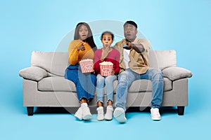 Surprised young family watching television with popcorn sitting on sofa