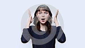 Surprised young female with open mouth big eyes raised hands on white background