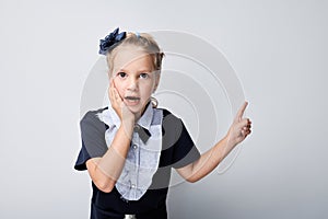 Surprised young girl points finger at gray background, expressing shock and amazement