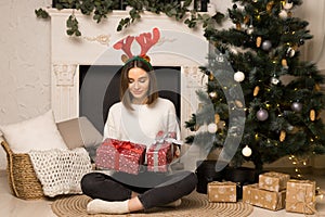 A surprised young girl sits and looks at two red Christmas gifts near the white fireplace