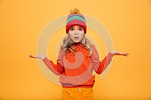 Surprised Young girl in sweater and hat shrugs her shoulders