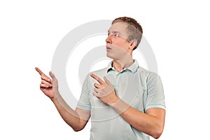 Surprised man with funny face in grey T-shirt pointing finger to left, white background