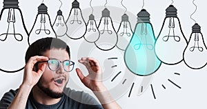 Surprised young guy with glasses, having new idea, looking at light bulb above his head on background of white color.