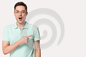 Surprised young man pointing at copy space for advertisement text.