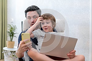 Surprised young man sit on computer using laptop relax with preschooler son have fun together, dad and little boy child