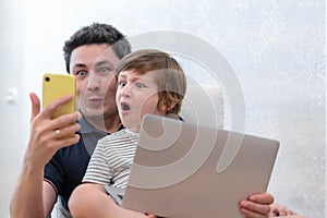 Surprised young man sit on computer using laptop relax with preschooler son have fun together, dad and little boy child enjoy
