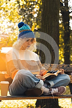 surprised young millennial girl reading book on bench in park - medium shot