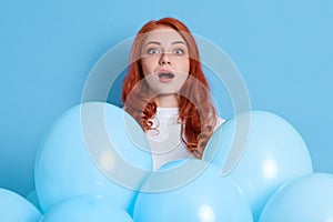 Surprised young red haired woman girl dresses white shirt, posing isolated on blue background. Birthday holiday party. Female with