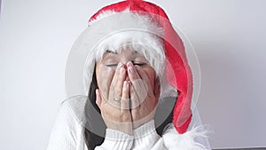 Surprised young Santa woman in a white sweater, Christmas hat, opens her mouth in surprise on a white background. Happy