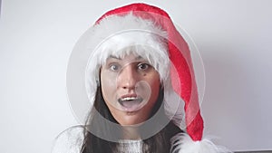 Surprised young Santa woman in a white sweater, Christmas hat, opens her mouth in surprise on a white background. Happy