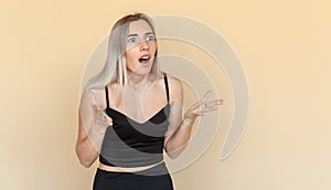 Surprised young woman with amazement face and open-mouthed. Shocked girl looking aside. Indoor studio shot on beige background