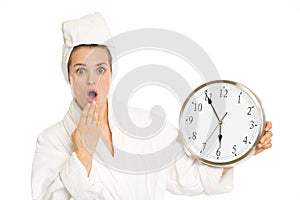 Surprised young woman in bathrobe with clock