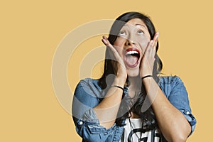 Surprised young woman with head in hands looking up over colored background