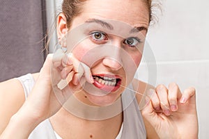 Surprised young woman holding dental floss caring and cleaning teeth