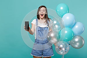 Surprised young woman holding mobile phone with blank empty screen, celebrating with colorful air balloons isolated on