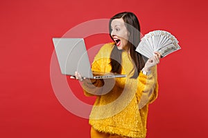 Surprised young woman keeping mouth wide open, hold laptop pc computer, fan of money in dollar banknotes, cash money