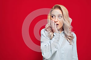 Surprised young woman looking to side, isolated on red background. Disbelief expression face of a cute girl. Wao - omg concept