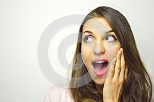 Surprised young woman looking to the side with open mouth with hand on the face on white background. Excited girl looking to the s