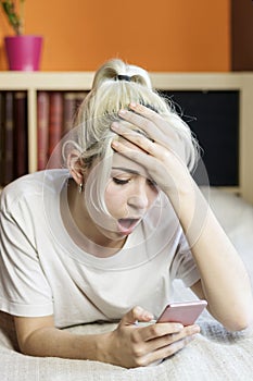 Surprised young woman lying on the bed while reading a phone mes