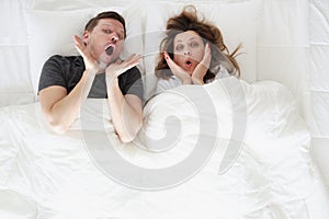 Surprised young woman and man lying in bed top view