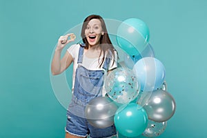 Surprised young woman with opened mouth holding bitcoin, future currency, celebrating with colorful air balloons