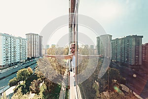 Surprised young woman pointing out something and looking to camera while on a window with the city as the background