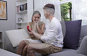 Surprised young woman with raising her hands and smiling while her boyfriend proposing her . Emotional couple in love.