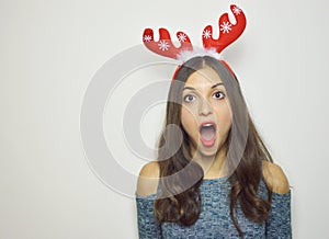 Surprised young woman with reindeer horns on her head with mouth open on white background