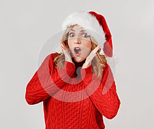Surprised Young woman in santa hat holding hands near face