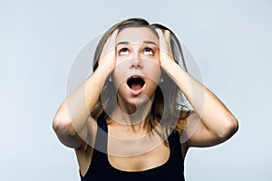 Surprised young woman screaming and putting her hands on her head looking at camera isolated on white.